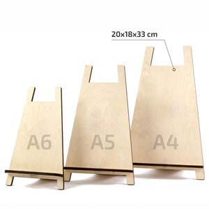 May include: Three wooden display stands in varying sizes, labelled A6, A5, and A4. The stands are made of light-coloured wood with a natural finish. The largest stand measures 33 cm high, 18 cm wide, and 20 cm deep.