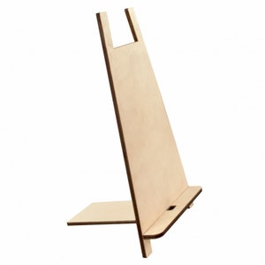 May include: A light-coloured wooden book stand with a rectangular base and a slanted back. The stand has a slot at the bottom to hold a book or tablet. The top has a cutout to hold a device in place. The stand is made of unfinished wood.