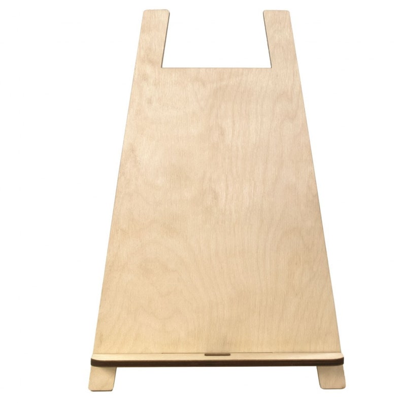 May include: A light-coloured wooden easel with a rectangular base and a wide, angled body. The top features a cutout handle. The wood grain is visible, and the easel is designed to hold items for display.