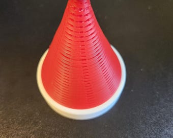 Puede incluir: Un objeto cónico impreso en 3D que se asemeja a un gorro de Papá Noel, con una textura acanalada de color rojo vibrante en el cono principal, una base circular blanca sólida y una pequeña punta esférica blanca en el vértice, con líneas de capa visibles.