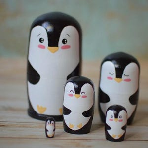 May include: A set of five nesting wooden penguin figurines. The penguins are painted black and white with cute cartoon faces. The largest penguin is about 10 inches tall.