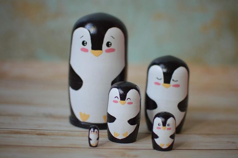 May include: A set of five nesting wooden penguin figurines. The penguins are painted black and white with cute cartoon faces. The largest penguin is about 10 inches tall.