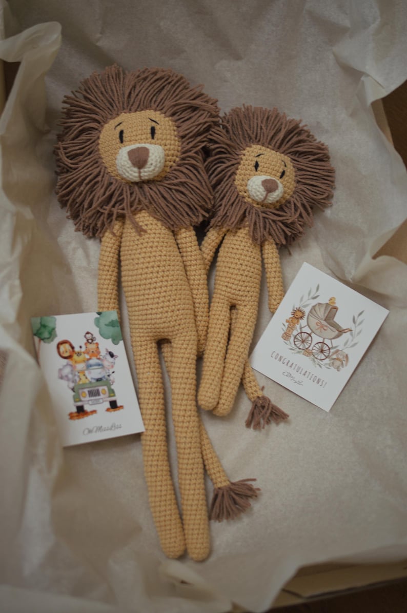 May include: Two handmade crochet lion stuffed animals with brown manes and tan bodies. The lions are holding hands. Two greeting cards are included, one with a safari scene and the other with a baby carriage and the word "Congratulations!"