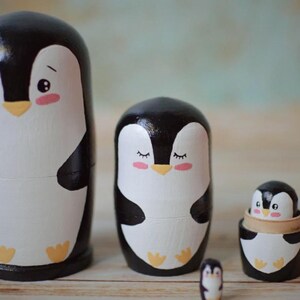 May include: Set of five nesting painted wooden penguin figurines. The largest penguin is black and white with a yellow beak and feet. The penguins get progressively smaller, with the smallest penguin being about the size of a thumb.