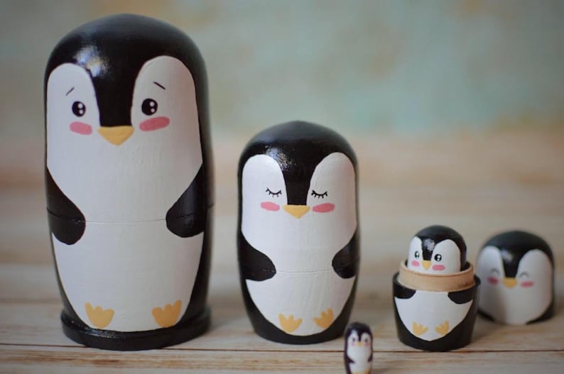 May include: Set of five nesting painted wooden penguin figurines. The largest penguin is black and white with a yellow beak and feet. The penguins get progressively smaller, with the smallest penguin being about the size of a thumb.