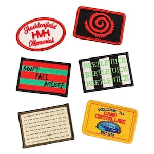 May include: A set of six embroidered iron-on patches featuring various designs and text. The patches include a red and white spiral design, a black and white striped patch with the text "Beetlejuice" repeated three times, a red and green patch with the text "Don't Fall Asleep", a yellow patch with the text "Welcome to Camp Crystal Lake Est. 1936", and two patches with text related to Haddonfield and HMH Memorial.