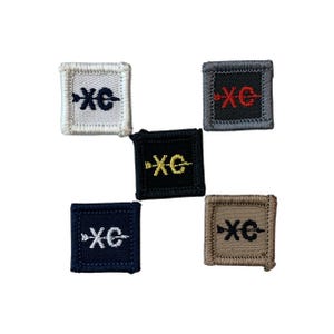May include: Five square embroidered patches in various colors: white, black, navy, gray, and tan. Each patch features the letters "XC" in a contrasting color, with a stylized arrow. The patches are likely for athletic or academic recognition.