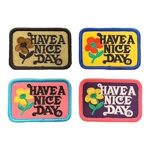 May include: Four embroidered patches with the text "HAVE A NICE DAY" and a flower design. The patches are in various color combinations: olive green, yellow, pink, and purple, each with a different coloured border.
