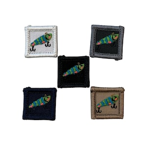 May include: Five square embroidered patches featuring a colorful fish lure design. The patches have a variety of background colors, including white, black, navy, gray, and tan. Each patch has a black hook.