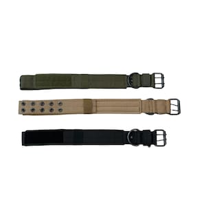 Pode incluir: Três cintos táticos em verde oliva, bege e preto. Cada cinto possui uma fivela e um anel em D de metal. O cinto verde oliva tem um patch de velcro. O cinto bege tem vários ilhós. Todos os cintos estão em um fundo branco.