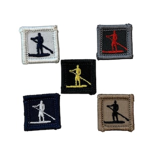 Könnte beinhalten: Eine Sammlung von fünf quadratischen, gestickten Aufnähern. Jeder Aufnäher zeigt eine Silhouette einer Person beim Stand-Up-Paddling. Die Aufnäher sind in verschiedenen Farben erhältlich, darunter Weiß, Grau, Schwarz, Marineblau und Beige. Die Silhouette des Paddlers ist in Kontrastfarben gehalten.