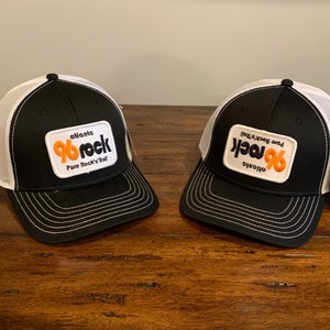 Könnte beinhalten: Zwei schwarze und weiße Trucker-Caps mit weißem Netzrücken. Die Caps haben einen schwarzen Patch auf der Vorderseite mit dem Text "Atlanta 96 Rock Pure Rock 'n' Roll".