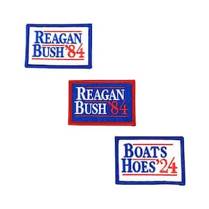 以下が含まれることがあります： 3つの長方形の刺繍パッチ。2つのパッチには、青い背景に白と赤の文字で「REAGAN BUSH '84」と書かれています。3つ目のパッチには、青い背景に白と赤の文字で「BOATS HOES '24」と書かれています。