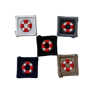May include: Five square patches featuring a red and white life preserver design. The patches have different colored backgrounds: white, black, navy blue, grey, and tan. The life preserver is centered on each patch.