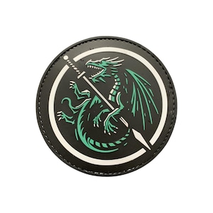 May include: A round, black patch featuring a green dragon design with a sword. The dragon is in the center, with a white outline and a white ring around the edge. The dragon has green wings and is holding a sword.