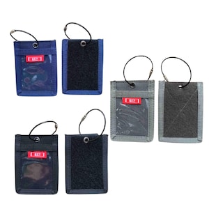 May include: A selection of ID badge holders in navy, black, and grey. Each holder has a clear window for an ID, a hook, and a Velcro patch. The holders feature a red label with white text.