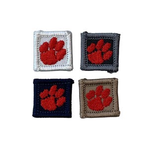 May include: Four square patches with a red paw print design. Each patch has a different colored border: white, gray, navy blue, and tan. The paw print is a vibrant red color.