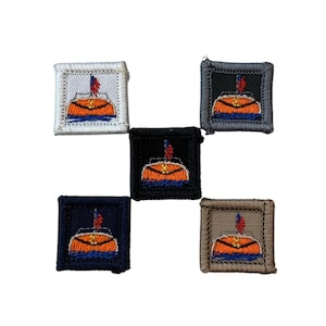 Può includere: Cinque toppe ricamate con un disegno di barca. Ogni toppa ha un bordo quadrato in bianco, nero, blu navy, grigio e marrone. La barca è arancione con onde blu, una bandiera rossa e uno sfondo bianco.