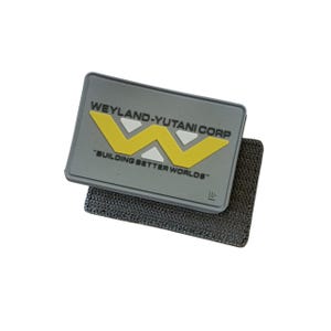 May include: A rectangular gray patch with the text "WEYLAND-YUTANI CORP" and "BUILDING BETTER WORLDS" in yellow and white. The patch features a yellow "W" logo and a black hook-and-loop fastener backing.