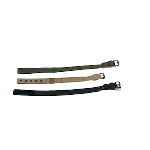 May include: Three dog collars in different colors: olive green, tan, and black. Each collar has a metal buckle and a strap for adjustment. The collars are displayed against a white background.