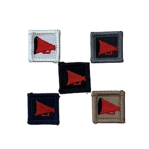 May include: Five embroidered square patches featuring a red megaphone design. The patches are in white, grey, black, navy, and beige. Each patch has a stitched border and a megaphone in the centre.