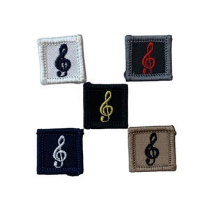 Pode incluir: Cinco patches quadrados com símbolos de clave de sol bordados. Os patches são em várias cores: branco, preto, azul marinho, bege e cinza. As claves de sol são em preto, vermelho e amarelo.