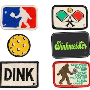 Puede incluir: Cinco parches bordados que representan una pelota de pickleball amarilla, dos palas de pickleball, un parche verde y negro con el texto "Dinkmeister", un parche blanco con el texto "DINK", y un Bigfoot marrón sosteniendo una pelota de pickleball con el texto "Keep your falafel out of my kitchen you volley llama Spwatch".