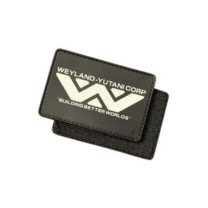 May include: A black rectangular patch with the text "WEYLAND-YUTANI CORP" and "BUILDING BETTER WORLDS" in white. The patch has a white stylized "W" logo and a hook-and-loop backing for attachment.