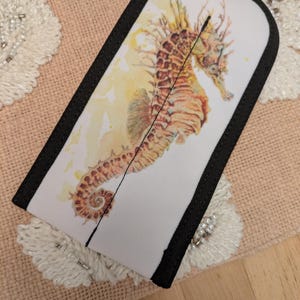 May include: A white and black seahorse-themed sleeve. The sleeve features a watercolor-style seahorse illustration in shades of orange, brown, and yellow. The sleeve has a black border and a vertical seam down the center.