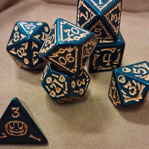 Könnte beinhalten: Eine Sammlung von Würfeln für Tabletop-Spiele. Die Würfel sind dunkelblau mit orange-gelben Zahlen und Designs. Die Würfel haben verschiedene Formen, darunter D4, D6, D8, D10, D12 und D20.
