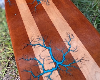 Könnte beinhalten: Ein langes Skateboard aus Holz mit drei Streifen aus hellem und dunklem Holz. Das Board hat ein blaues und schwarzes Blitzmuster.
