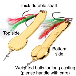 May include: Two gold fishing lures with red and green feathers. The lures have weighted balls for long casting. The text "Thick durable shaft" and "Weighted balls for long casting (please handle with care)" is visible. The text "208" is visible on one of the lures.