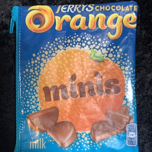 May include: A blue zippered pouch with a Jerry's Chocolate Orange Minis design. The pouch features a large orange with the word "minis" in brown text. The pouch also has the text "Jerrys Chocolate Orange" and "milk" in white text.