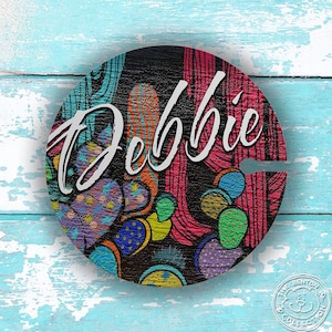 May include: A round wooden sign with a black background and a colorful cactus design. The name "Debbie" is written in white cursive lettering on the sign.