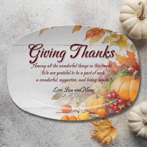 May include: An oval serving platter with a Thanksgiving theme. The platter features the text "Giving Thanks" and a message. It is decorated with pumpkins, fall leaves, and berries. The background is white with a wood grain pattern.