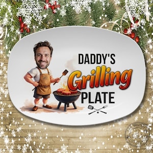 May include: White oval platter with the text "DADDY'S Grilling PLATE" and a cartoon illustration of a man grilling. The man is wearing an apron that says "JAKE". A spatula and fork are crossed below the text.