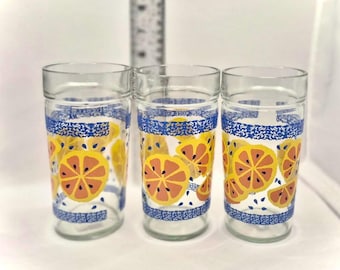 Könnte beinhalten: Drei transparente Gläser mit einem Zitrusfrucht-Design. Die Gläser haben ein blau-weiß gemustertes Band oben und unten, mit orangefarbenen und gelben Zitrusfruchtscheiben, die die Seiten verzieren. Die Gläser sind zylindrisch.