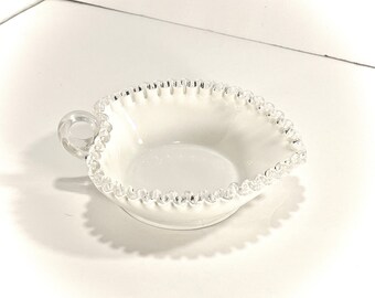 May include: A white milk glass bowl with a beaded edge and a single handle. The bowl is perfect for serving small snacks or desserts.
