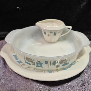 May include: A vintage white serving dish set with a matching creamer. The set features a light blue and gray pattern around the edges. The creamer is placed on top of the serving dish, which sits on a matching plate.