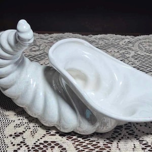 Może przedstawiać: Biała ceramiczna cornucopia z kręconym wzorem. Cornucopia ma kształt rogu i szeroki, otwarty otwór.