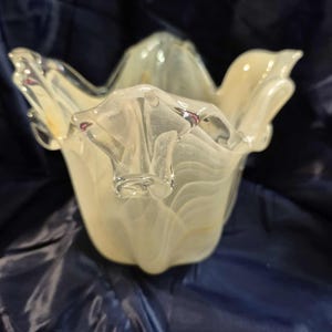 May include: A clear and off-white glass bowl with a unique, organic shape. The bowl has a flared, petal-like design with a textured, swirled pattern. The glass has a translucent quality, allowing light to pass through.