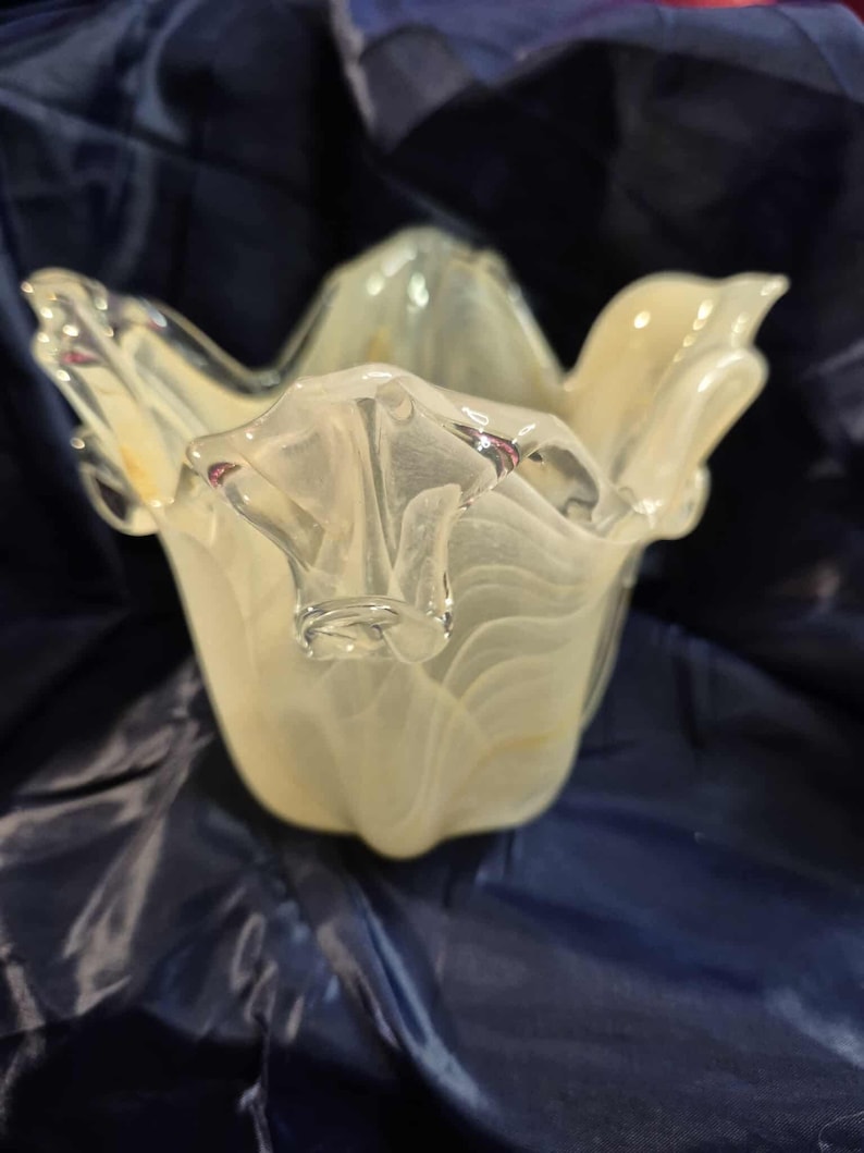 May include: A clear and off-white glass bowl with a unique, organic shape. The bowl has a flared, petal-like design with a textured, swirled pattern. The glass has a translucent quality, allowing light to pass through.