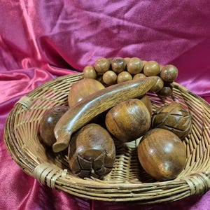 May include: A woven basket filled with various wooden objects. The basket contains several round, carved wooden spheres, a long, curved wooden piece, and a strand of wooden beads. The objects are displayed on a pink satin fabric.