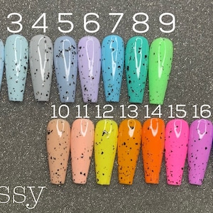 May include: Eighteen long, oval-shaped fake nails with a glossy finish. Each nail is painted a different color with black speckles. The nails are numbered 1 through 18.