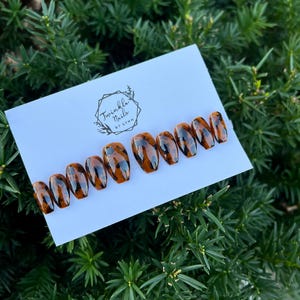 May include: Set of ten tortoise shell press-on nails with a brown and black pattern. The nails are arranged on a white card with the text "Twinkle Nails by Lynn".