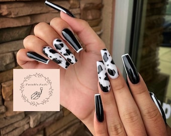 May include: Long, black and white cow print nails with a white tip and black polish on the other nails.