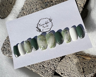 May include: Green and white marble-effect press-on nails with silver glitter accents. The nails are arranged on a white card with the text "Twinkle Nails by Lynn".