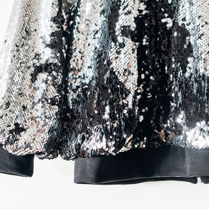 May include: A black and silver sequined jacket with a black ribbed knit cuff and hem.