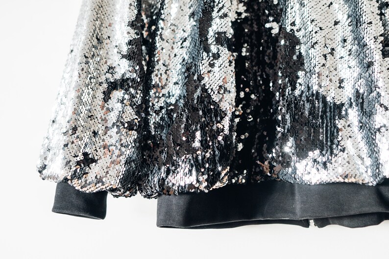 May include: A black and silver sequined jacket with a black ribbed knit cuff and hem.
