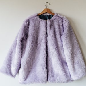 May include: A lavender faux fur jacket hanging on a wooden hanger.